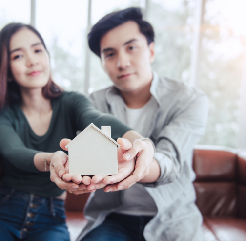 A couple holding a small wood home, showing the possible benefits of applying for a joint personal loan