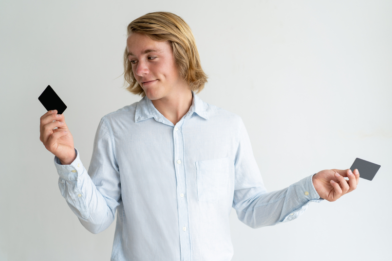 A man holding a credit card in each hand weighing the pros and cons of credit cards.