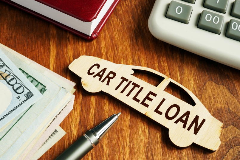 a small wooden car on a desk, with cash, a pen, and a calculator within view.