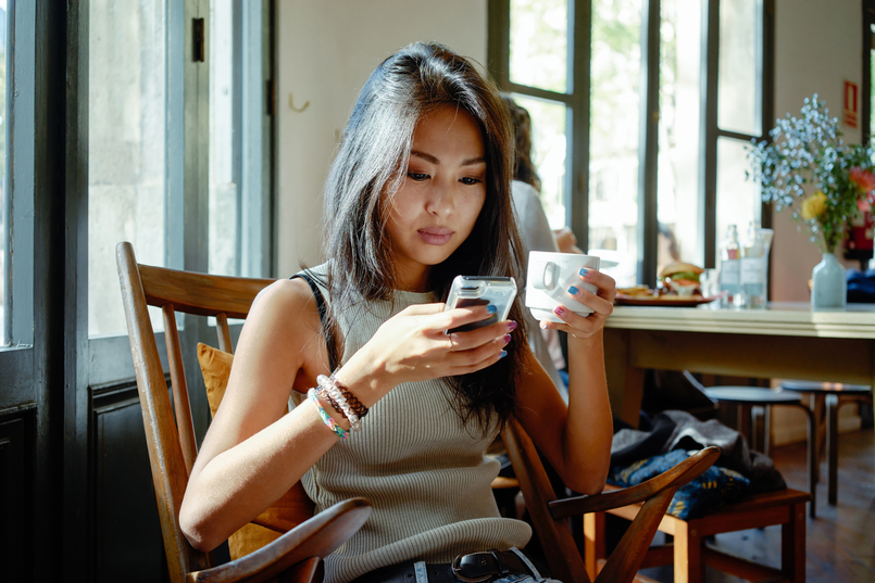 an attractive young asian woman researching when the credit score was invented on her phone in a coffee shop
