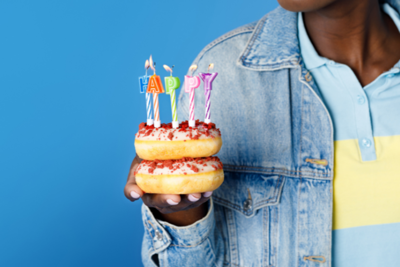 a woman holding two donuts she got for free on her birthday with lit happy birthday candles on top