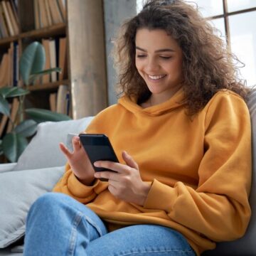 Young woman wearing a yellow hoodie scrolling on a smart phone