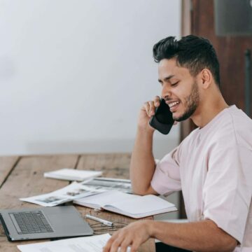 man on phone with documents and laptop managing personal finances.