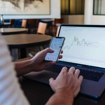 Person using phone and laptop to invest.